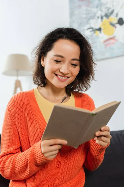 Mujer feliz y tatuada leyendo libro en casa - foto de stock