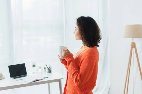 Vista laterale della giovane donna soddisfatta che tiene la tazza a casa — Foto stock