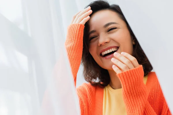 Portrait of cheerful young woman laughing near white curtain — Stock Photo