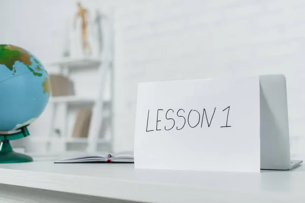 Paper with lesson one lettering near globe and notebook on desk — Stock Photo