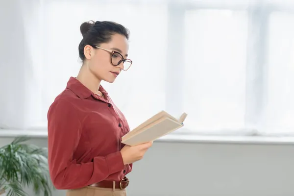 Junge Lehrerin in Brille liest Buch — Stockfoto