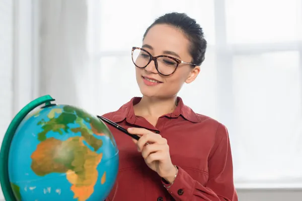 Cheerful teacher in eyeglasses holding pen near globe — Stock Photo
