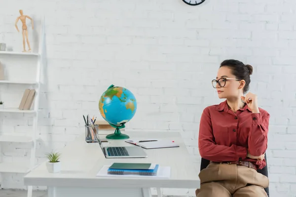 Jeune professeur en lunettes regardant ordinateur portable sur le bureau — Photo de stock