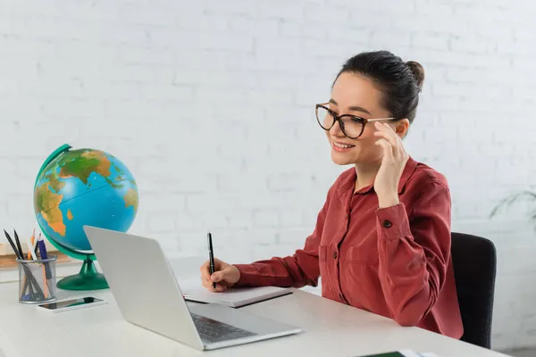 Giovane insegnante sorridente in occhiali che guarda il computer portatile sulla scrivania — Foto stock