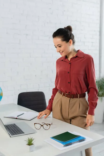 Souriant jeune professeur regardant ordinateur portable sur le bureau — Photo de stock