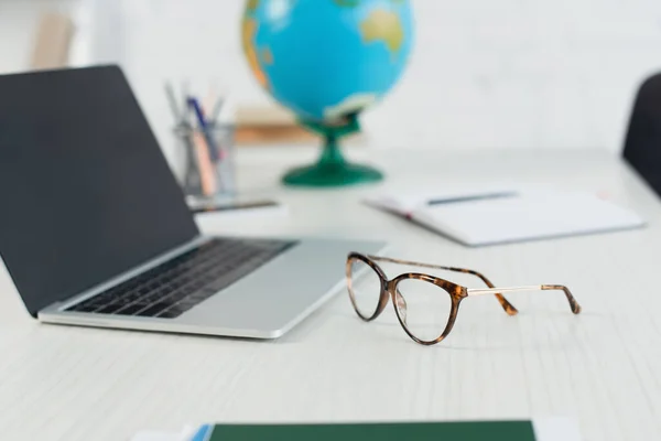 Glasses near blurred laptop with blank screen on desk — Stock Photo