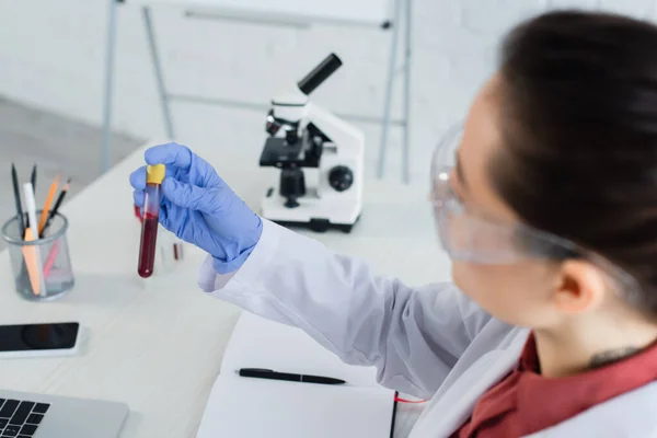 Young scientist in latex glove and goggles holding test tube with blood — Stock Photo