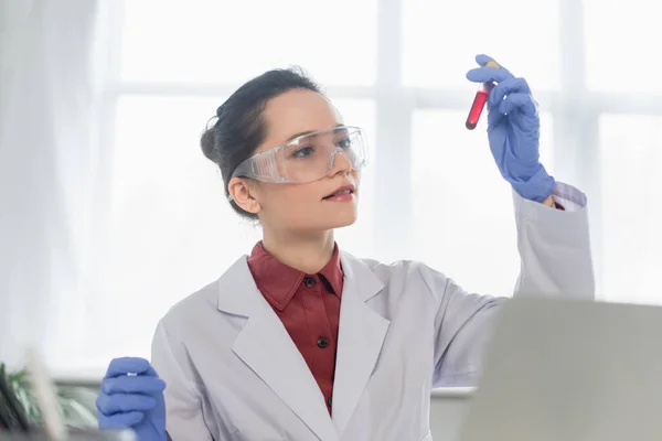 Jeune scientifique en gants et lunettes en latex tenant un tube à essai avec du sang — Photo de stock