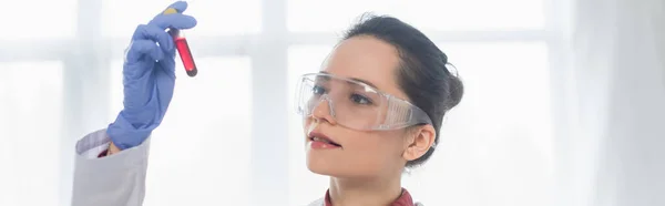 Jeune scientifique en gant de latex et lunettes tenant le tube à essai avec du sang, bannière — Photo de stock