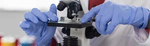 Cropped view of scientist in latex gloves near microscope, banner — Stock Photo