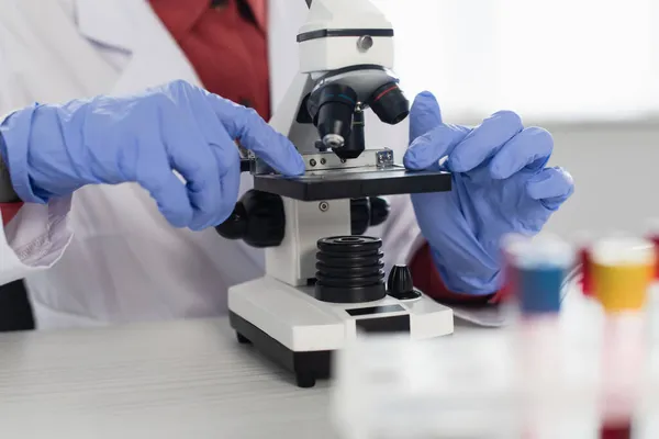 Vista recortada de científico en guantes de látex cerca del microscopio - foto de stock