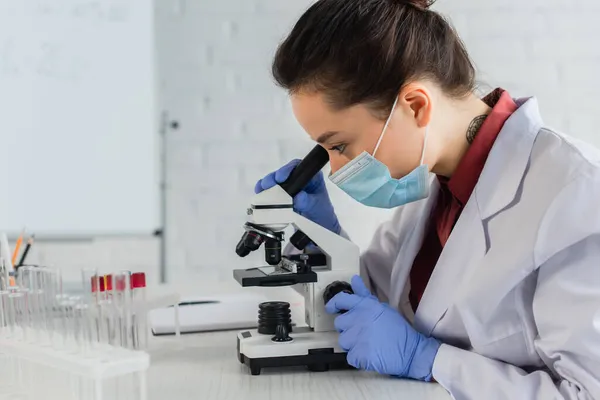 Scientifique tatoué dans des gants de latex regardant à travers le microscope en laboratoire — Photo de stock