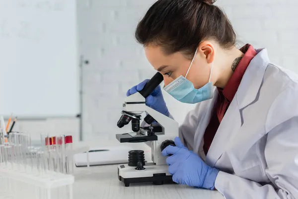 Tattooed scientist in latex gloves looking through microscope in laboratory — Stock Photo