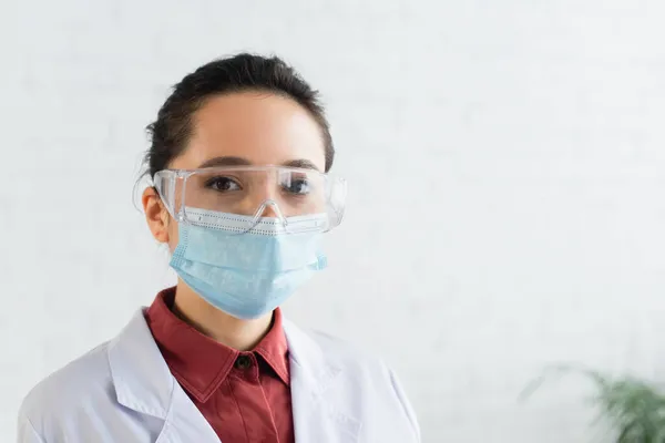 Brünette Wissenschaftlerin mit Brille und medizinischer Maske blickt im Labor in die Kamera — Stockfoto