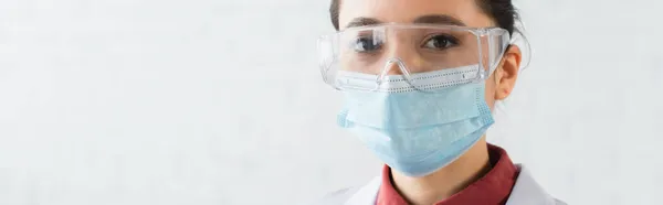 Brünette Wissenschaftlerin mit Brille und medizinischer Maske blickt in die Kamera im Labor, Banner — Stockfoto