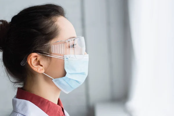 Vista laterale di bruna scienziato in occhiali e maschera medica — Foto stock