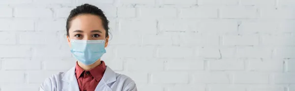 Brunette doctor in medical mask looking at camera, banner — Stock Photo