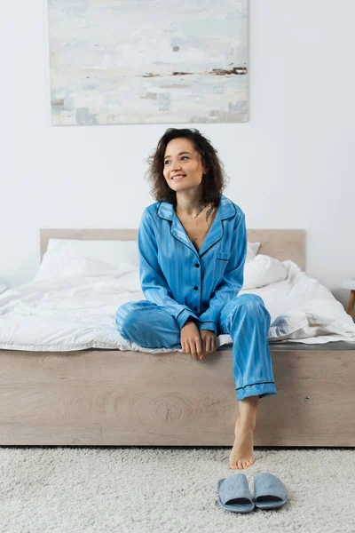 Glücklich tätowierte Frau im Pyjama auf dem Bett sitzend — Stockfoto