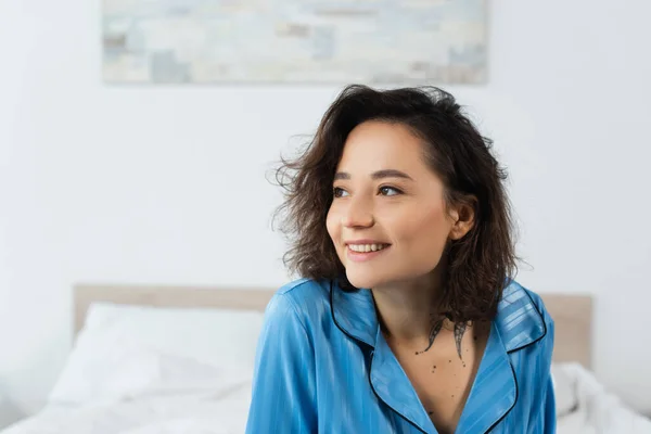 Glückliche und tätowierte Frau im blauen Pyjama, die zu Hause wegschaut — Stockfoto