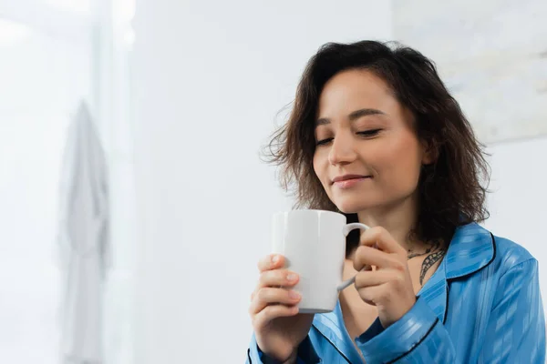 Femme heureuse en pyjama bleu tenant tasse de café dans la chambre — Photo de stock