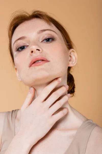 Portrait of redhead woman touching neck isolated on beige — Stock Photo