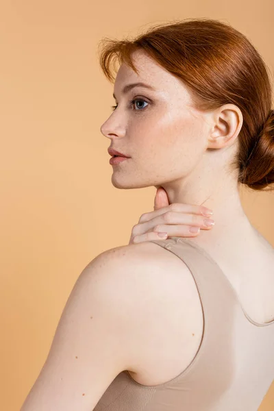 Bella donna dai capelli rossi toccare il collo e distogliere lo sguardo isolato sul beige — Foto stock