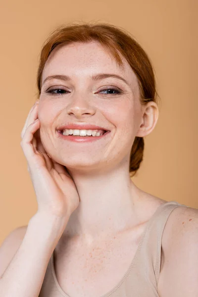 Retrato de una bonita mujer pelirroja sonriendo y mirando hacia otro lado aislada en beige - foto de stock