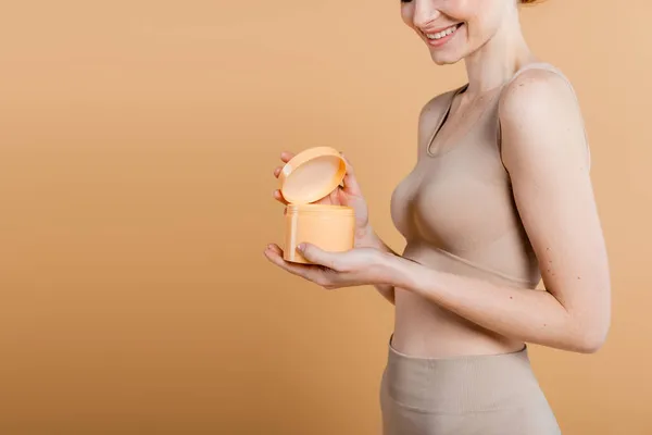 Cropped view of smiling woman in top holding cosmetic cream isolated on beige — Stock Photo