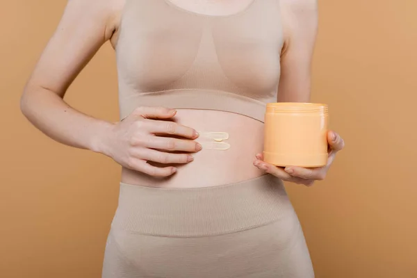 Cropped view of woman in top applying cosmetic cream isolated on beige — Stock Photo