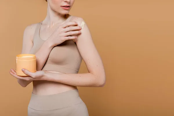 Vista recortada de la mujer pecosa aplicando crema aislada en beige - foto de stock