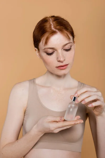 Sommersprossige Frau im Oberteil schaut sich das auf Beige isolierte kosmetische Serum an — Stockfoto