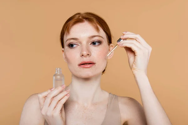 Pretty woman with freckled skin applying cosmetic serum isolated on beige — Stock Photo