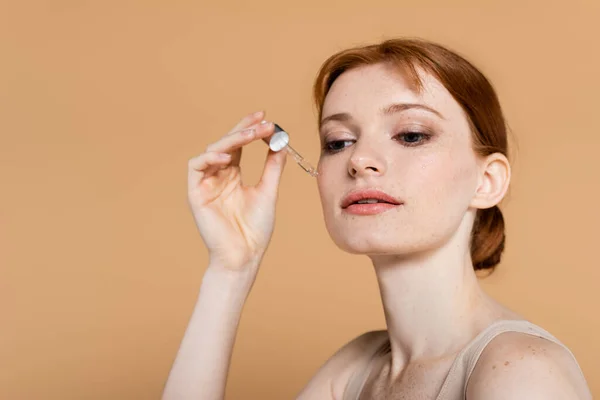 Hübsche Frau mit sauberer Haut unter Anwendung kosmetischen Serums isoliert auf beige — Stockfoto