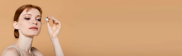 Jolie femme appliquant le sérum cosmétique de la pipette isolé sur beige, bannière — Photo de stock