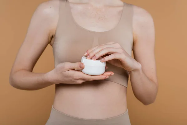 Cropped view of woman in top holding container with cream isolated on beige — Stock Photo