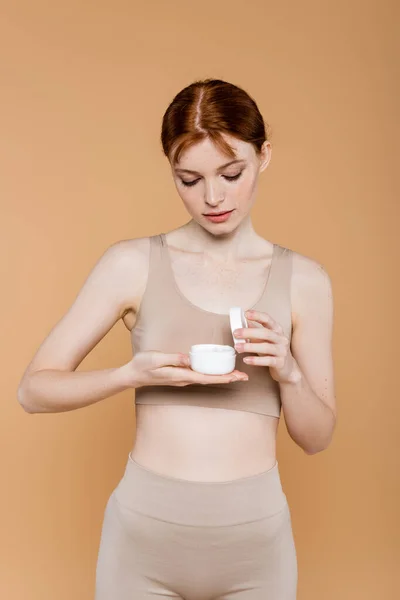 Freckled woman in top looking at cosmetic cream isolated on beige — Stock Photo