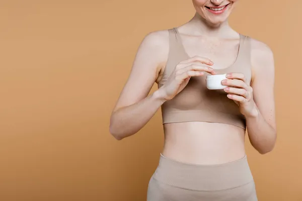 Cropped view of smiling freckled woman in top holding cosmetic cream isolated on beige — Stock Photo