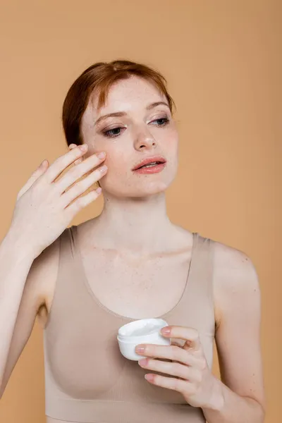 Jeune femme en haut appliquant de la crème sur le visage isolé sur beige — Photo de stock