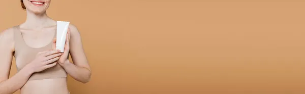Vue recadrée du tube de maintien femme taches de rousseur positive avec lotion isolée sur beige, bannière — Photo de stock