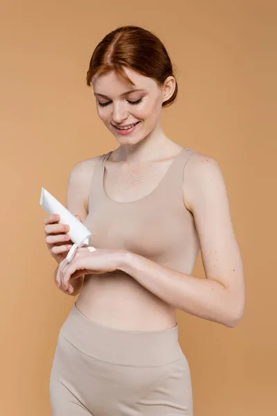 Mulher alegre no topo aplicando creme na mão isolado no bege — Fotografia de Stock