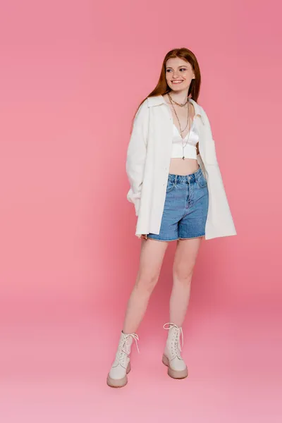 Full length of smiling red haired woman looking away on pink background — Stock Photo