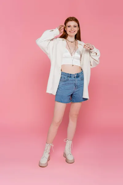 Mujer pelirroja feliz en chaqueta sonriendo a la cámara sobre fondo rosa - foto de stock