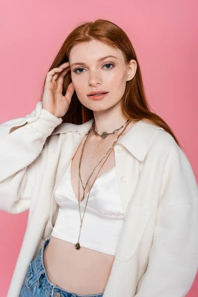 Young redhead woman in jacket and necklaces posing isolated on pink — Stock Photo