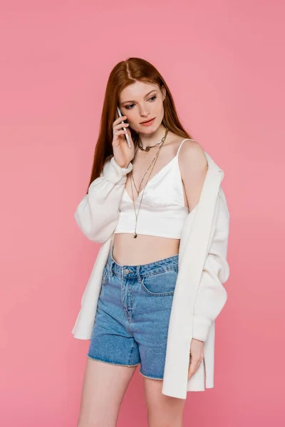 Mujer elegante con la piel pecosa hablando en el teléfono inteligente aislado en rosa - foto de stock