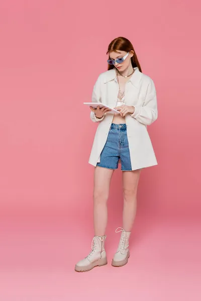Полная длина молодой стильной женщины, использующей цифровую табличку на розовом фоне — стоковое фото