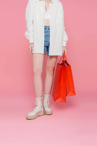 Vue recadrée de jeune femme élégante tenant des sacs à provisions sur fond rose — Photo de stock