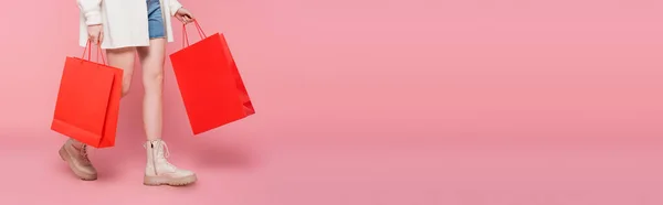 Vista recortada de la mujer con bolsas de compras caminando sobre fondo rosa, pancarta - foto de stock