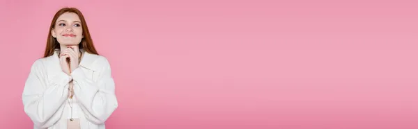Mujer pelirroja alegre en chaqueta mirando hacia otro lado aislado en rosa, pancarta - foto de stock