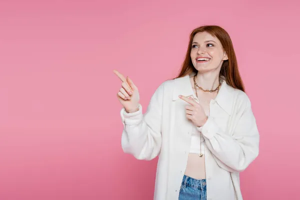 Smiling redhead woman pointing with fingers isolated on pink — Stock Photo