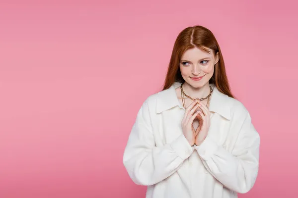 Sly red haired woman in jacket and necklaces looking away isolated on pink — Stock Photo